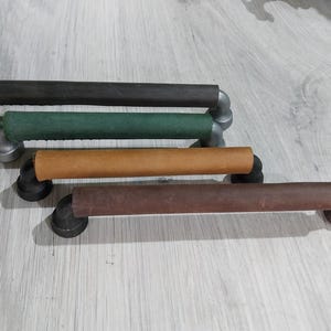 Puede incluir: Cuatro tiradores de armario de estilo industrial con diseño de tubería y cuero. Los tiradores presentan una combinación de metal y cuero en varios colores: marrón oscuro, verde, beige y marrón. Los herrajes son de metal.
