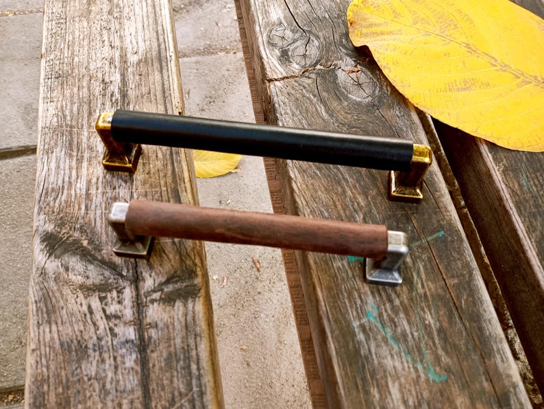 May include: Two cabinet door pulls, one black and one brown wood. The black pull has gold accents. The brown pull has silver accents.