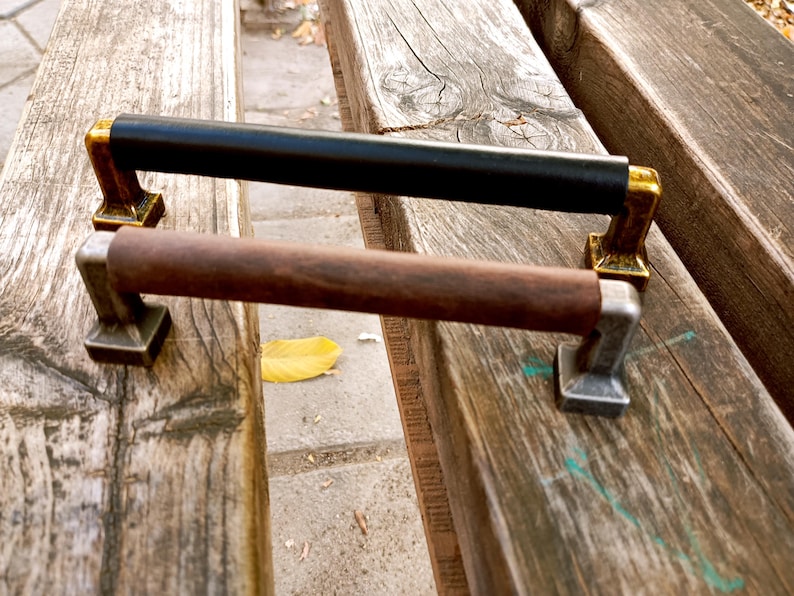 May include: Two cabinet door pulls, one with a black leather handle and gold accents, and the other with a brown wooden handle and silver accents.