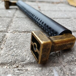 May include: A black leather cabinet pull with a stitched design and a brass base.