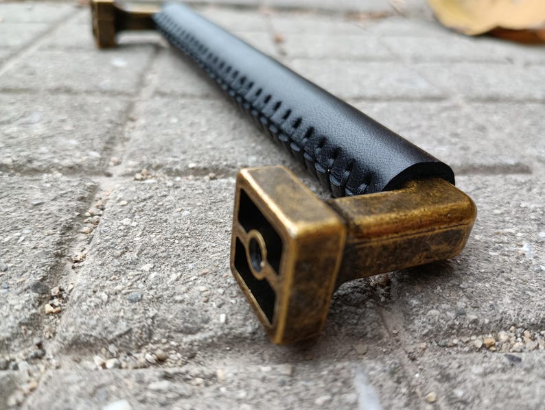 May include: A black leather cabinet pull with a stitched design and a brass base.