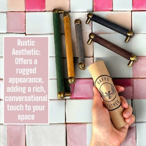 May include: Five different colored leather cabinet pulls with brass accents. The pulls are arranged on a pink and white tiled surface. A hand is holding a brown tube with the text "GAFFO LEATHER" printed on it.