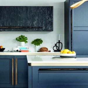 May include: A modern kitchen with dark blue cabinets and gold hardware. The cabinets have a wood grain finish and are accented with black handles. The countertop is white with a gold trim.