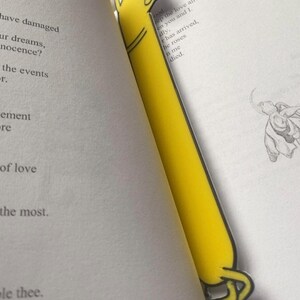 Peut inclure: Un marque-page jaune en forme de chien de dessin anim&eacute; avec une patte lev&eacute;e. Le marque-page est sur une page d'un livre avec le texte "keep the love alive" et "he roses in me died."