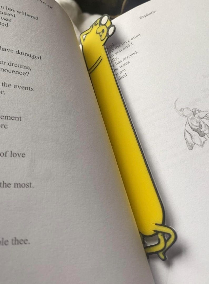 Peut inclure: Un marque-page jaune en forme de chien de dessin anim&eacute; avec une patte lev&eacute;e. Le marque-page est sur une page d'un livre avec le texte "keep the love alive" et "he roses in me died."
