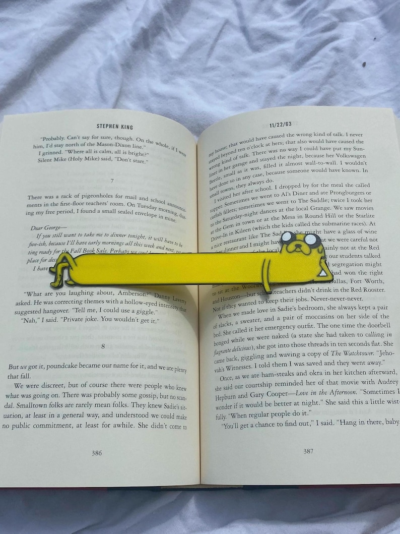 Peut inclure: Un gros plan d'un livre ouvert avec un signet jaune repr&eacute;sentant un chien de dessin anim&eacute;. Le livre est intitul&eacute; "Stephen King" et le texte sur la page dit "Probably Can't say for sure, though. On the whole, if I were him, I'd stay north of the Mason-Dixon line."