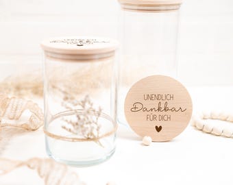 Könnte beinhalten: Zwei Glasgläser mit Holzdeckeln und einem Holz-Kreis mit dem Text "Unendlich Dankbar Für Dich". Die Gläser sind leer und haben einen rustikalen Look.
