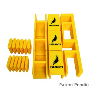 May include: Bright yellow 3D-printed modular building blocks. The blocks include rectangular and L-shaped pieces, along with blocks with the text "F3DPRINTS" and a feather logo. The words "Patent Pending" are also visible.
