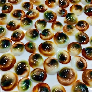 May include: A collection of numerous smooth, oval-shaped cabochons featuring a swirling pattern of deep brown, forest green, and creamy white colors. Each piece has a polished, glossy finish that reflects light, creating a uniform appearance.