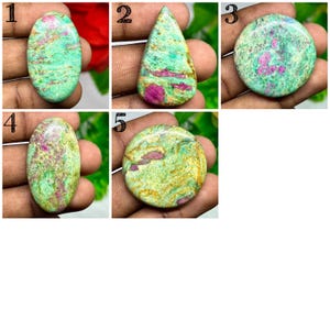 May include: A collection of five polished gemstones, each with a unique shape. The stones feature a mix of green, pink, and gold hues, with visible patterns and textures. The gemstones are oval, teardrop, and round.