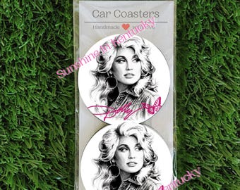 May include: Two round car coasters in a clear plastic sleeve. Each coaster features a black and white portrait of a woman with voluminous hair, wearing hoop earrings and a denim jacket. The name Dolly is written in pink script with a pink butterfly.