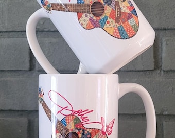 May include: Two white ceramic mugs stacked vertically, each featuring a colorful patchwork quilt pattern on an acoustic guitar graphic. The design includes the word Dolly in pink script above the guitar and a small pink butterfly to the right side.