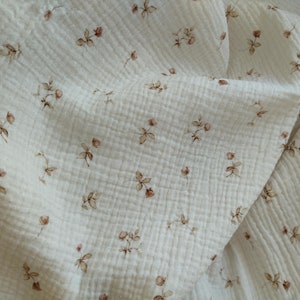 Peut inclure: Tissu blanc avec un motif floral délicat en brun. Le tissu a une apparence texturée, semblable à une gaufre.