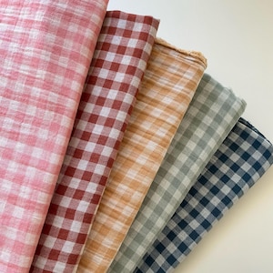 May include: Five fabric samples in a range of colours, each with a gingham check design. The colours are pink, red, orange, grey-green, and navy blue. The fabric has a slightly textured appearance.