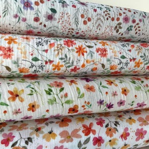 Op de afbeelding: Vier rollen bloemenstof in verschillende designs. De stof heeft een witte achtergrond met kleurrijke bloemen in tinten oranje, roze, paars en rood. De stof is waarschijnlijk katoen of een vergelijkbaar materiaal.