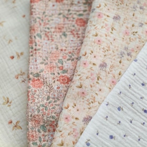 May include: Close-up of four different floral patterned fabrics. The fabrics feature various designs, including small flowers and leaves in shades of pink, peach, and purple on a cream or white background. The fabrics have a textured, crinkled appearance.