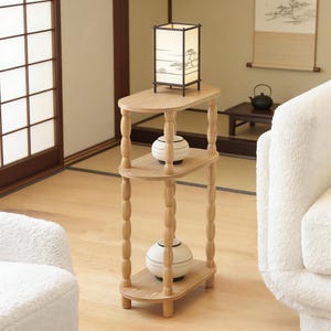 Puede incluir: Una mesa auxiliar de madera de tres niveles con tapa y estantes ovalados. La mesa tiene patas torneadas y sostiene una lámpara de estilo japonés y dos jarrones decorativos. La lámpara tiene un marco negro y una pantalla de papel con un diseño de paisaje.