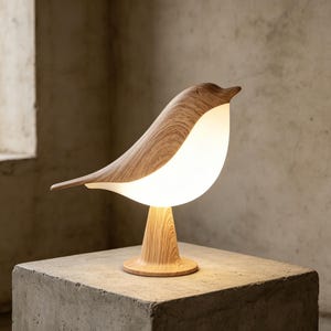 May include: A wooden bird-shaped table lamp with a warm, glowing light. The lamp features a light-colored wooden body with a white, illuminated belly. The lamp is on a wooden base, and the overall design is modern and decorative.