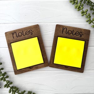 May include: Two wooden note holders with the word "Notes" engraved on the front. Each holder has a yellow sticky note inside.