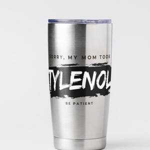 May include: A stainless steel tumbler with a black and white design. The text on the tumbler reads "SORRY, MY MOM TOOK TYLENOL BE PATIENT". The tumbler has a silver lid and a silver body.
