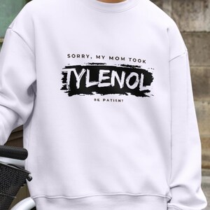 May include: White sweatshirt with the text "SORRY, MY MOM TOOK TYLENOL BE PATIENT" in black. The word "TYLENOL" is in a bold, distressed font. The sweatshirt is a casual style.