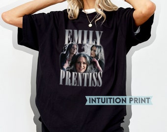 May include: Black t-shirt with a vintage-style graphic of Emily Prentiss from the TV show Criminal Minds. The graphic features a collage of three images of Emily Prentiss with the text "Emily Prentiss" in a bold, white font. The text "INTUITION PRINT" is printed in white on a blue banner at the bottom of the shirt.
