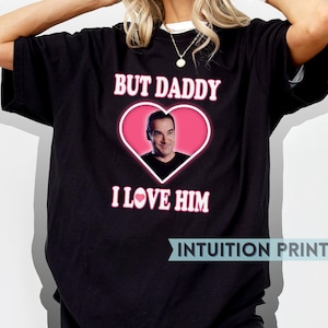 May include: Black t-shirt with a pink heart and the text "But Daddy I Love Him" printed on it. The heart features a photo of a man inside.