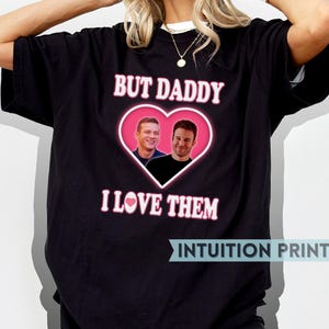Puede incluir: Camiseta negra con un gráfico de corazón rosa con dos hombres y el texto "But Daddy I Love Them".
