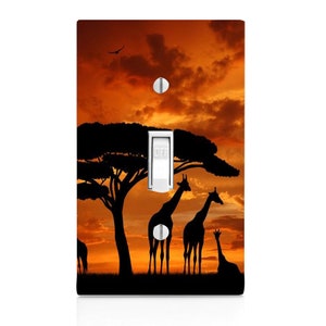 May include: A light switch cover with a silhouette of giraffes and a tree against an orange sunset sky.