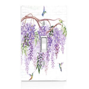 May include: A decorative light switch cover featuring a watercolor design of purple wisteria flowers and hummingbirds against a white brick background. The switch is in the "off" position.