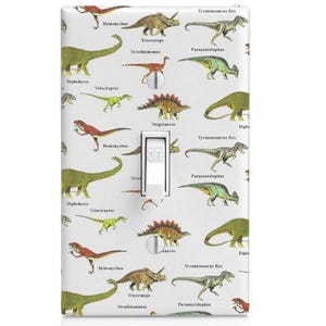 May include: A white light switch cover with a colorful dinosaur pattern. The cover features various dinosaurs, including a Tyrannosaurus Rex, Triceratops, Stegosaurus, and Parasaurolophus. Each dinosaur is labeled with its scientific name.