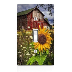 May include: A light switch cover featuring a red barn with a sunflower in the foreground. The barn is surrounded by green grass and white flowers. The switch is labeled "OFF".