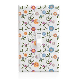 May include: A white light switch cover with a floral design. The design features orange, purple, and blue flowers with green leaves and vines. The switch is in the "off" position.