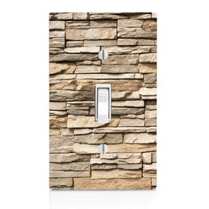 May include: A light switch cover with a stone wall design. The cover is beige and brown with a light switch that says "OFF".