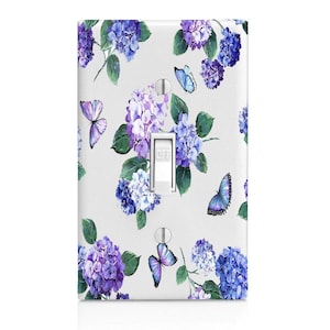 May include: A white light switch cover featuring a floral design with purple and blue hydrangeas and butterflies. The switch is in the "OFF" position. The design includes green leaves and a light gray background.