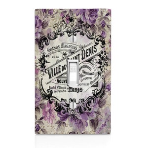 May include: A light switch cover with a vintage Parisian design featuring a floral pattern in shades of purple and gray. The text reads "Grands Magasins de la Ville de Saint Denis" and "Faubg S'Denis de Paradis Paris".