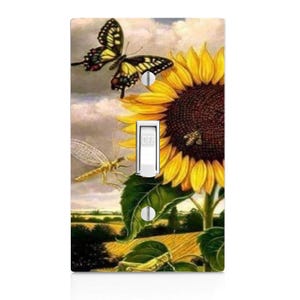 May include: A light switch cover featuring a vibrant sunflower with yellow petals and a dark brown center. A yellow and black butterfly is perched on the sunflower, and a dragonfly is flying nearby. The background is a soft blue sky with white clouds.