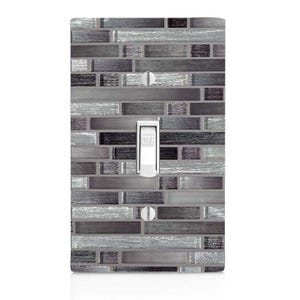 May include: A light switch cover with a gray and silver mosaic tile design. The switch is labeled "OFF".