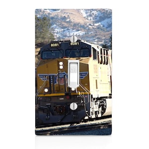 May include: A yellow and black Union Pacific train locomotive with the numbers 8081 on the front. The train is on a track with a mountain background.