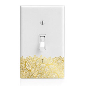 May include: A white light switch cover with a gold leaf design. The switch is in the off position.