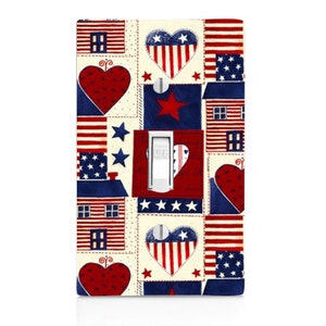 May include: A light switch cover with a patriotic design featuring red, white, and blue stars, hearts, and houses. The design is reminiscent of a patchwork quilt.