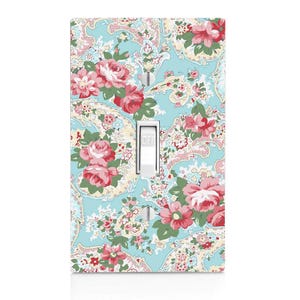 May include: A decorative light switch cover with a floral pattern. The cover features a light blue background with a paisley design and pink and red roses. The switch is white, with the word "OFF" printed on it.