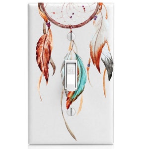 May include: White light switch cover featuring a watercolor dreamcatcher design. The dreamcatcher has a brown circular frame with hanging feathers in shades of orange, teal, and white. The switch is in the "OFF" position.