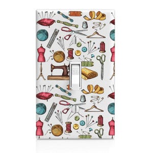 May include: A white light switch cover with a colorful pattern of sewing and tailoring tools. The pattern includes a sewing machine, scissors, spools of thread, buttons, needles, thimbles, and fabric.