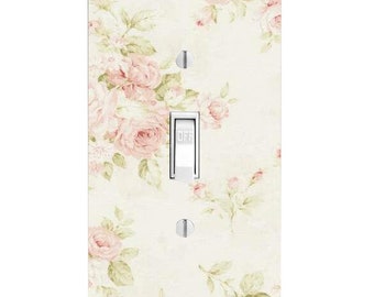 May include: A rectangular light switch cover plate featuring a cream-colored background with a pattern of soft pink roses and green leaves. The plate includes a central white toggle switch labeled OFF and two silver screws for mounting.