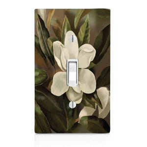 May include: A light switch cover with a floral design featuring white magnolia blossoms and dark green leaves. The switch is labeled "OFF".