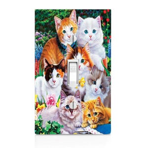 May include: A decorative light switch cover featuring a colorful illustration of several adorable cats. The cats have various fur colors, including orange, white, and calico, and are surrounded by flowers and greenery. The switch is in the "OFF" position.