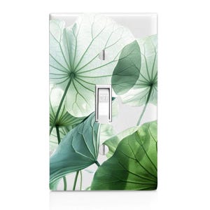 May include: A light switch cover with a design of overlapping green leaves. The leaves have a light green and dark green color scheme. The switch is labeled "OFF".