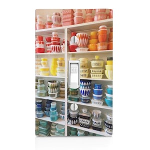 May include: A light switch cover featuring a photograph of a collection of vintage Pyrex bowls. The bowls are arranged on shelves and are in various colors, including red, orange, yellow, blue, and green. The switch is in the off position.