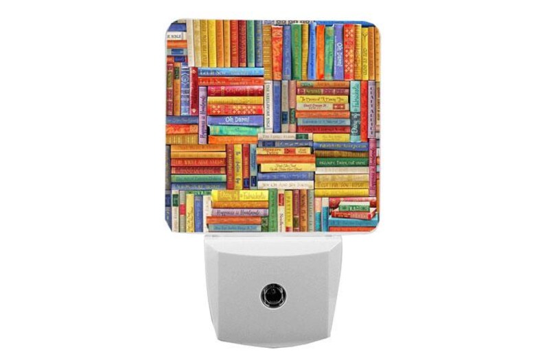 May include: A square night light featuring a colourful, multi-directional collage of book spines in various shades of red, blue, yellow, green, and orange. The design includes small text on several spines, set against a white plug-in base.